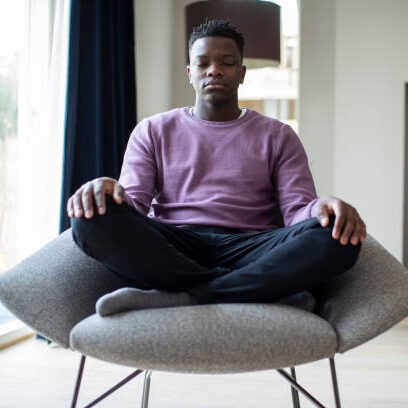 Close Up Of Peaceful Teenage Boy Meditating Sitting In Chair At Home